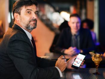 a man in a business suit sitting at bar with his cell phone